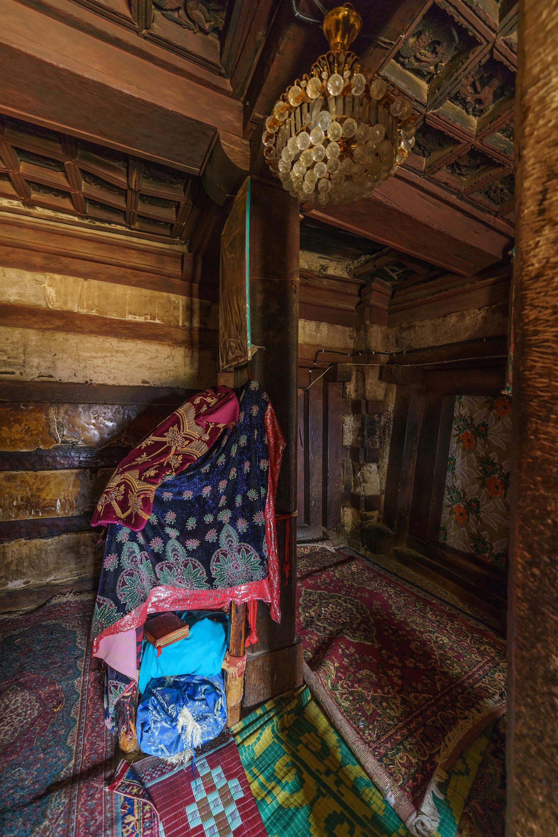 Colour interior photograph looking up into a deep timber coffered ceiling of square carved panels held in a heavy grid, above pale plastered walls banded with dark timbers, with vestments and carpets below