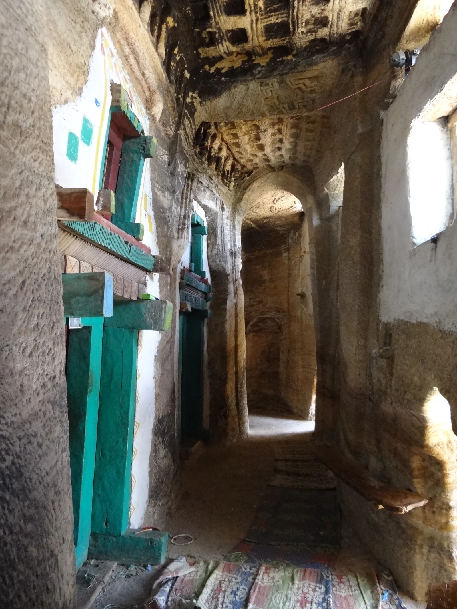 Madhane Alem Addi Qesho: long interior rock-cut passage with vaulting, floor rugs and painted timber doors.