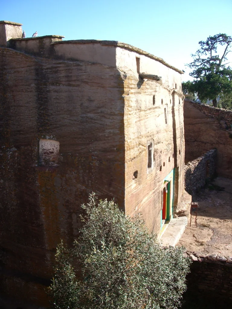 Mika'el Amba: elevated exterior showing the exposed rock-hewn facade, roof line, windows and doorway.