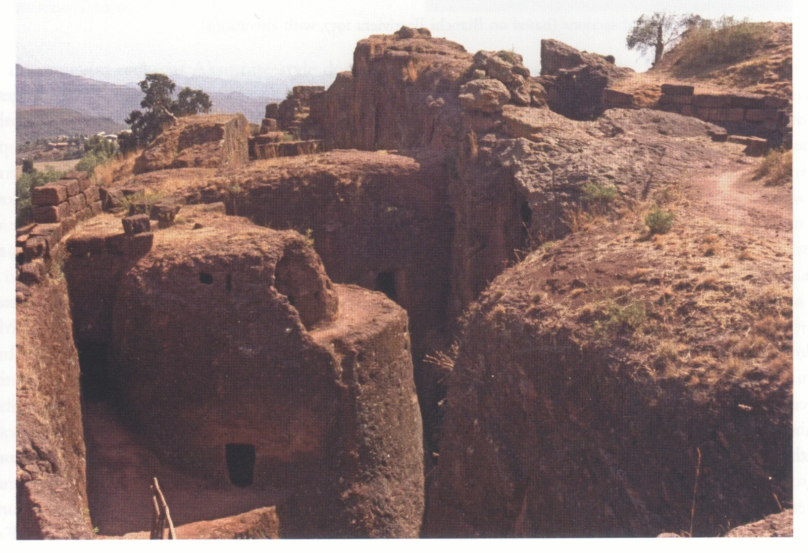 Bethlehem, exterior view from the northeast, 1998. The chamber seen in fig. 209 is inside the semi-isolated cylindrical rock seen in the left foreground, above which and to the left are remains of a wall built of large stone blocks. In the background, behind Bethlehem, the trapezoidal court of Beta Gabriel-Rafa’el is visible with, to the right, the wall protecting its northeastern entrance.